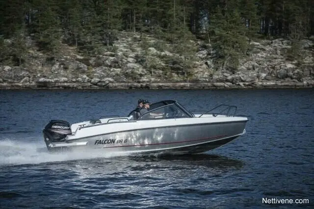 A sleek Falcon 8 boat speeds across a lake, with a man at the helm and lush forested shoreline in the background.